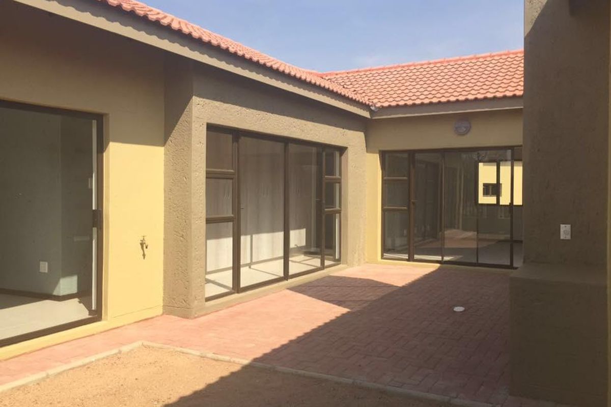 A private rear courtyard featuring paved flooring, terracotta roof tiles, and multiple sliding glass door access points to the interior living spaces.