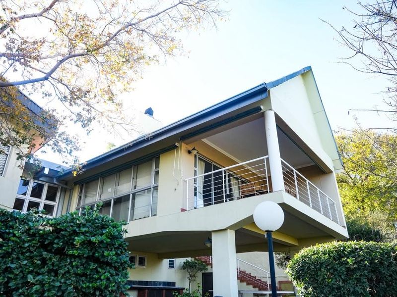 Rear view of the house featuring a spacious elevated balcony with metal railings and large sliding glass doors overlooking the garden.