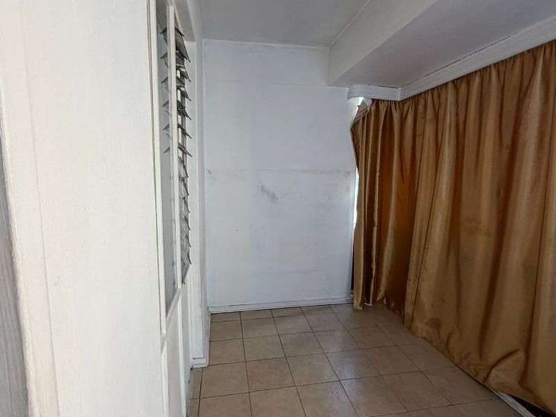 An empty, enclosed balcony or sunroom featuring tiled flooring and louvre windows, requiring cosmetic updates to the wall finishes.