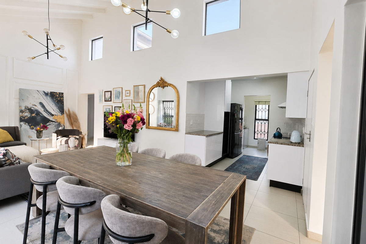 Spacious open-plan living and dining area featuring vaulted ceilings with exposed beams, clerestory windows, and a modern kitchen with stone countertops.