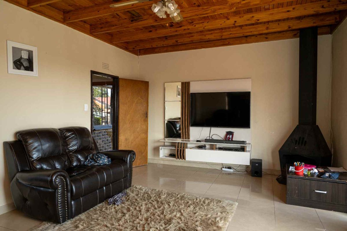A living room featuring a warm exposed timber ceiling, tiled flooring, and a prominent freestanding fireplace, creating a cozy and functional living space.