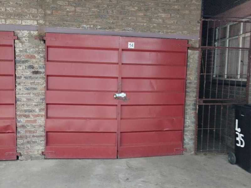 A functional garage space featuring red metal doors, brick exterior walls, and concrete flooring, providing secure parking or storage.