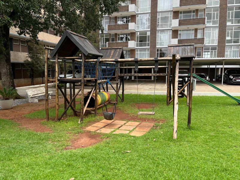 Communal garden area featuring a wooden playground structure set on a well-maintained lawn with paved access.
