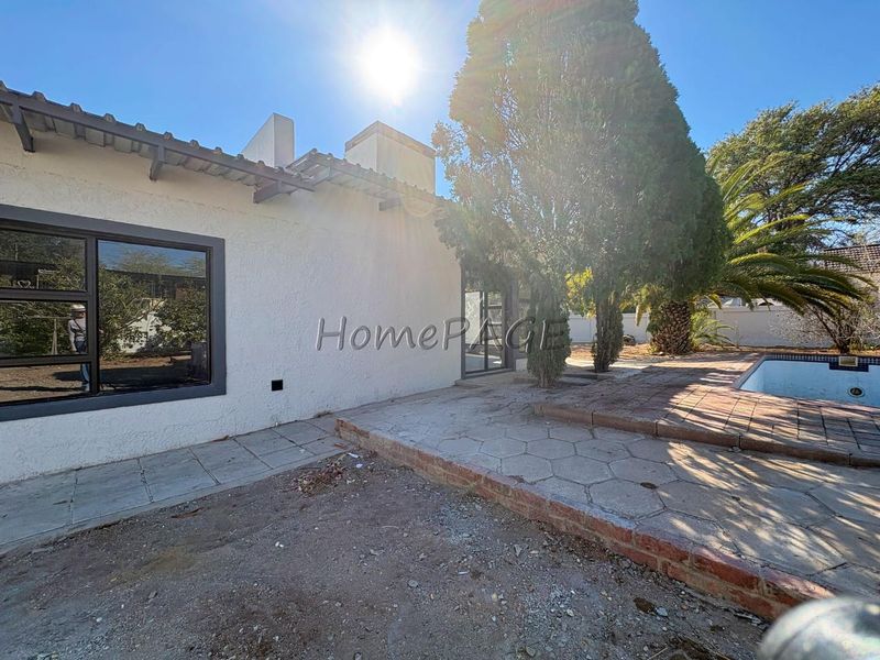 Rear exterior view of the property featuring a swimming pool, paved patio area, and established trees, requiring landscaping and maintenance.