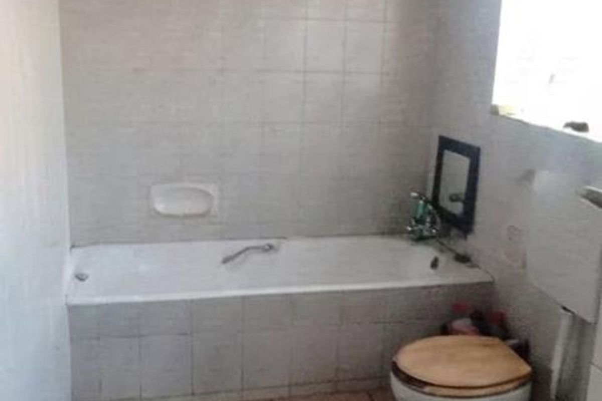 A dated bathroom featuring a built-in bathtub, toilet, and exposed timber ceiling, requiring cosmetic updates to improve its overall condition and appeal.