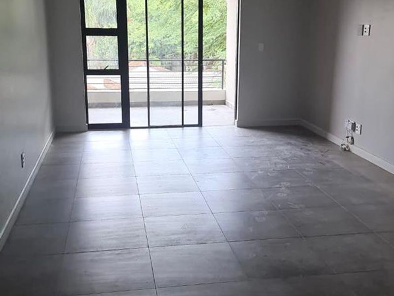 An empty, open-plan living area featuring large grey floor tiles, recessed lighting, and a sliding glass door leading to an outdoor balcony.
