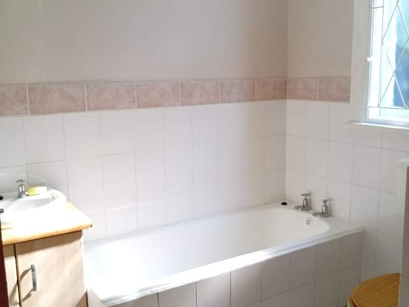 A functional bathroom featuring a built-in bathtub, vanity cabinet, and tiled finishes, illuminated by a leaded glass window.