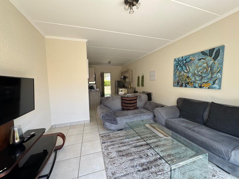 Open-plan living area featuring tiled flooring and a connected kitchen space with built-in cabinetry and an extractor fan.
