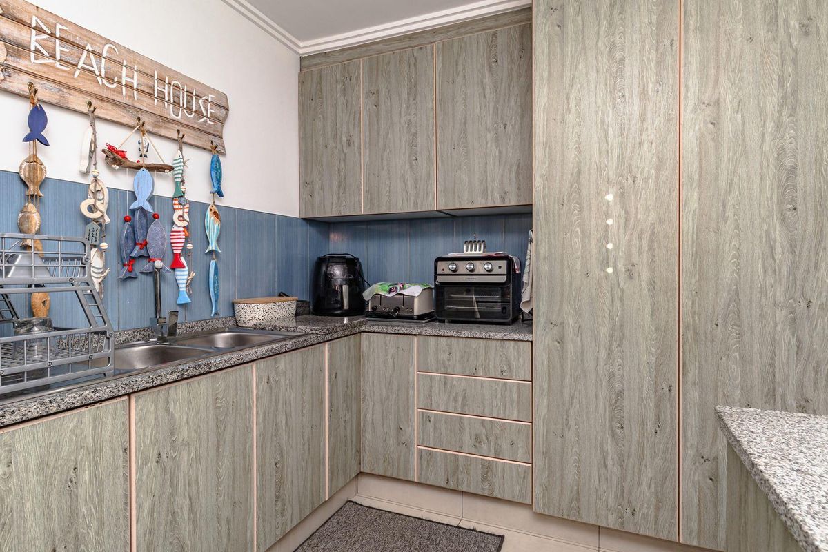 Compact kitchen featuring wood-grain laminate cabinetry, granite-look countertops, a double stainless steel sink, and blue tiled splashback.