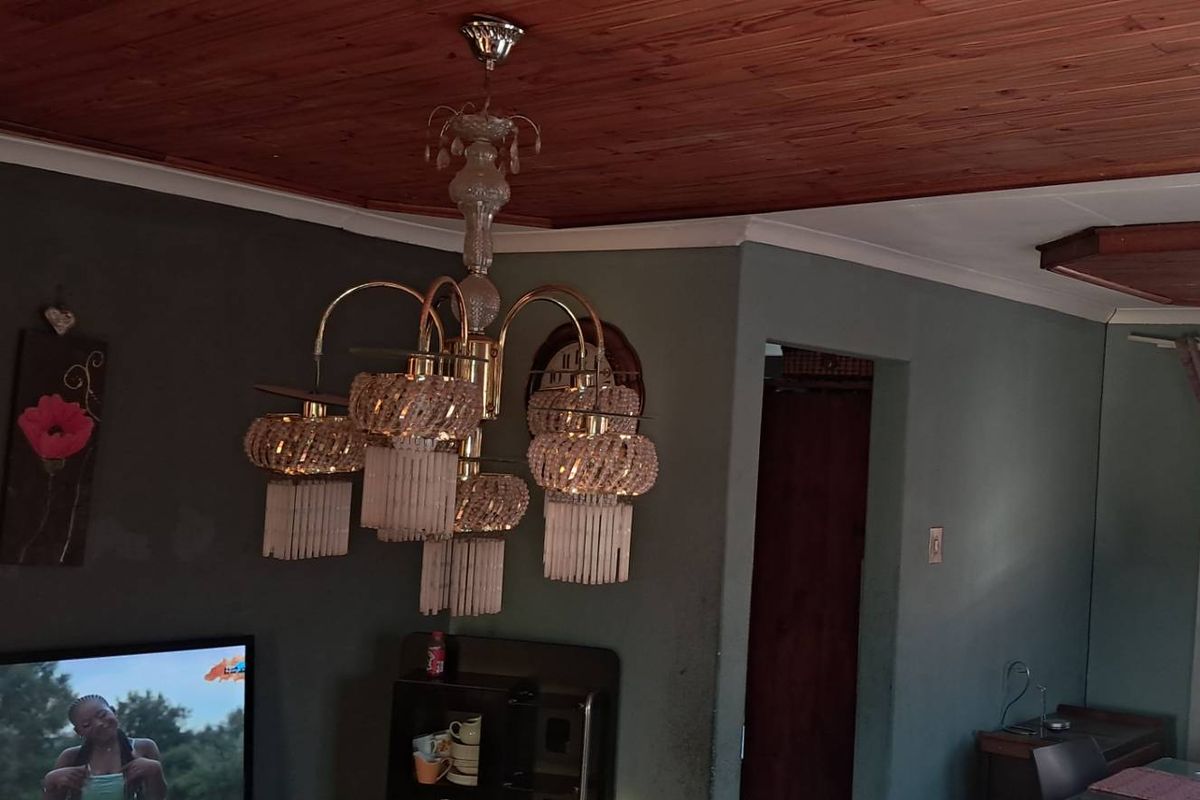 A living area featuring a timber-clad ceiling, decorative chandeliers, and dark-toned walls, providing a traditional aesthetic.