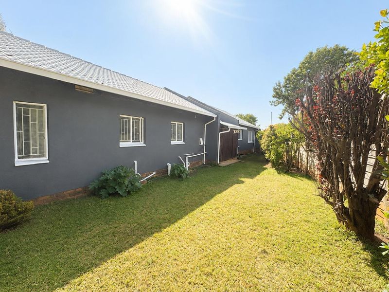 A view of the rear exterior of the house featuring a lawn, boundary wall, and tiled roof with security bars on the windows.