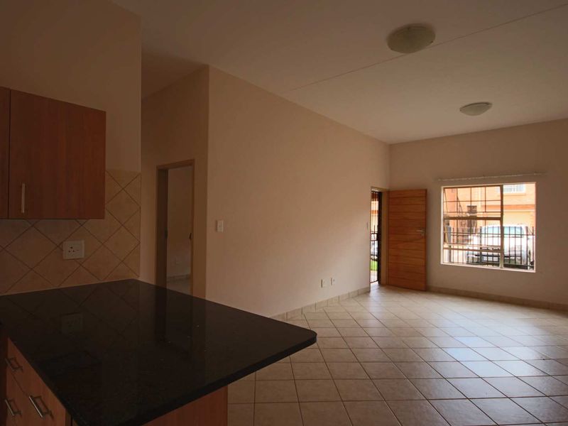 Open-plan living area featuring tiled flooring, granite kitchen countertops, and built-in cabinetry, with direct access to an exterior entrance and security-fitted windows.