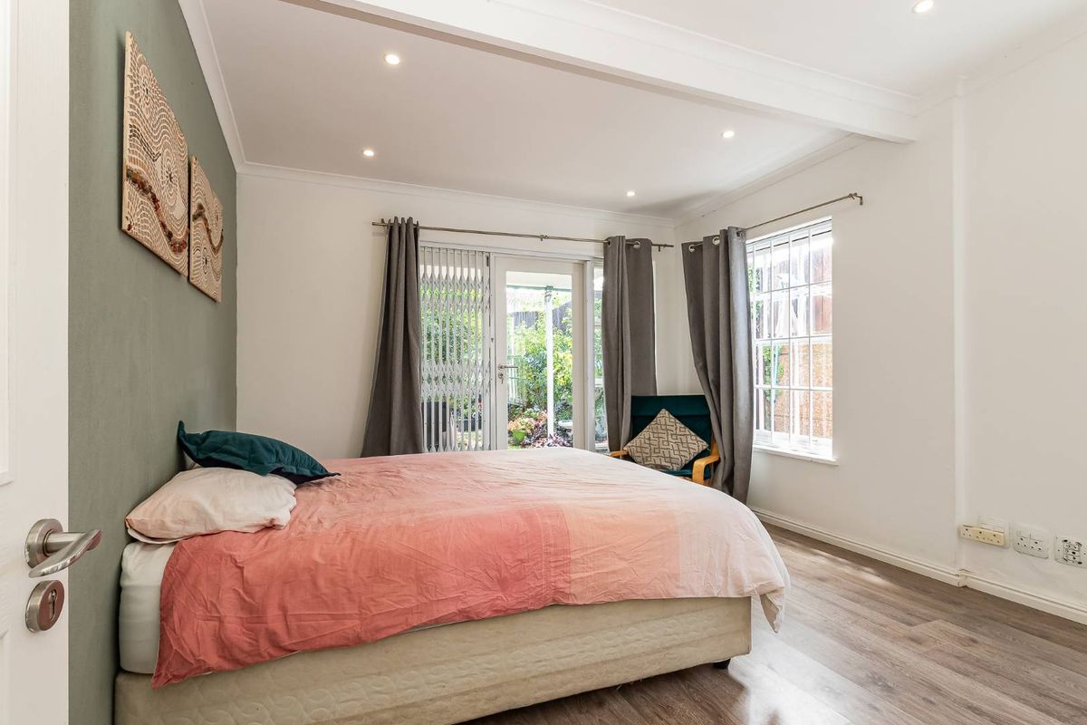 A bright bedroom featuring laminate flooring, recessed downlighting, and a sliding glass door providing direct access to the rear garden.