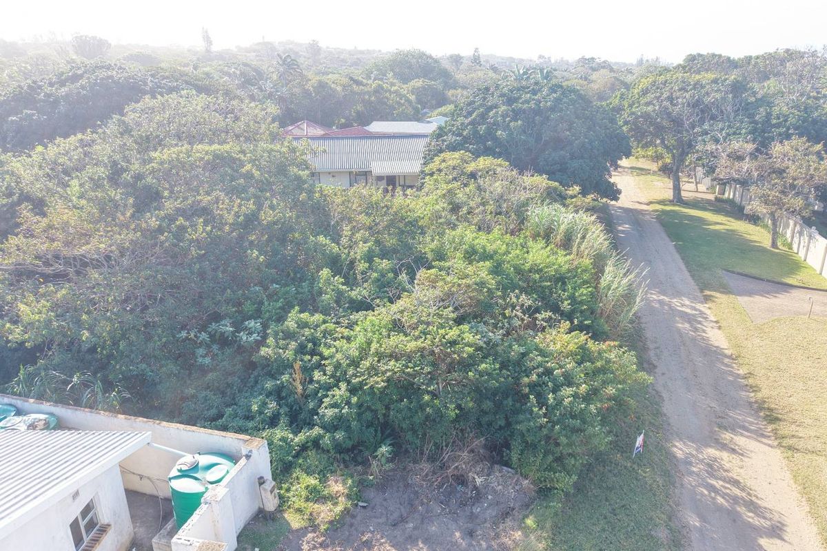 Aerial view of a vacant residential plot featuring dense vegetation, a dirt access road, and an adjacent boundary wall with a water tank.