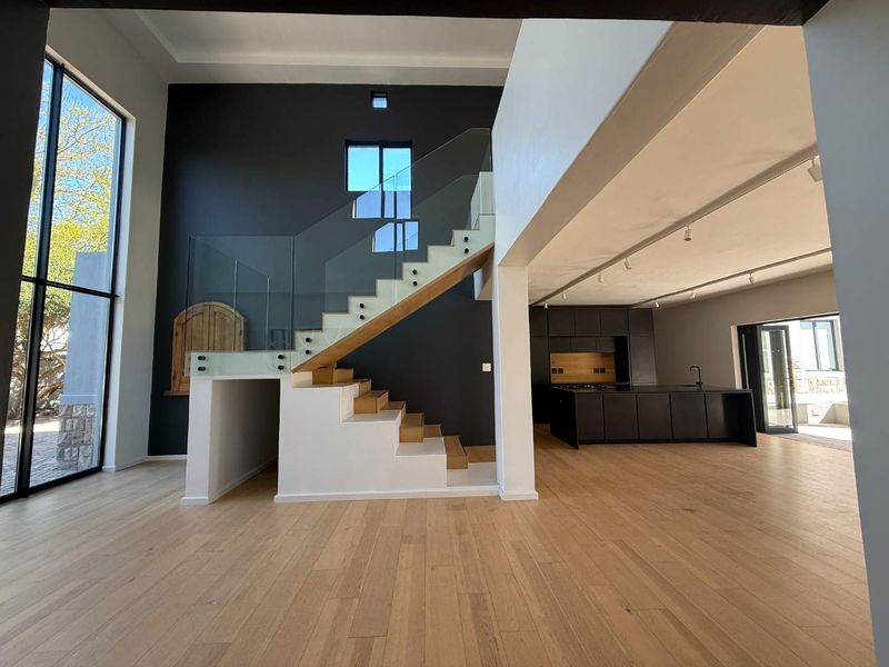 Spacious open-plan living area featuring a modern staircase with glass balustrades, timber flooring, and a sleek contemporary kitchen with dark cabinetry.