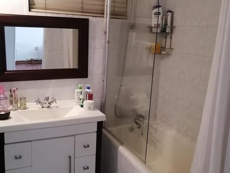A functional bathroom featuring a vanity cabinet with basin, a bathtub with a glass shower screen, and tiled finishes throughout.