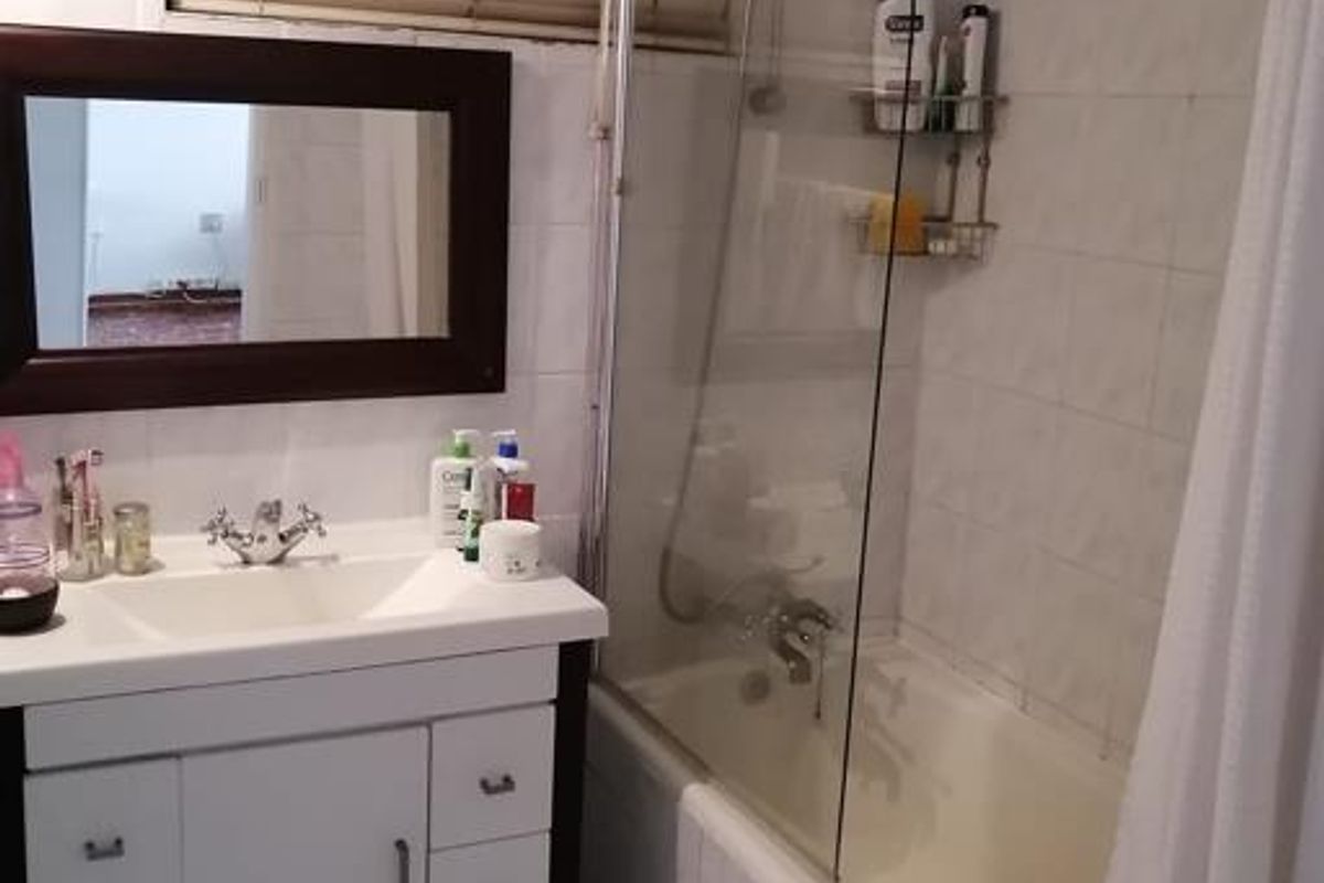 A functional bathroom featuring a vanity cabinet with basin, a bathtub with a glass shower screen, and tiled finishes throughout.