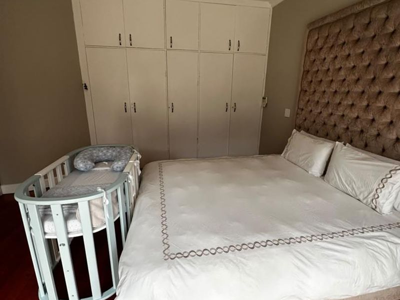 A well-maintained bedroom featuring polished hardwood flooring, built-in floor-to-ceiling cupboards, and recessed ceiling lighting.