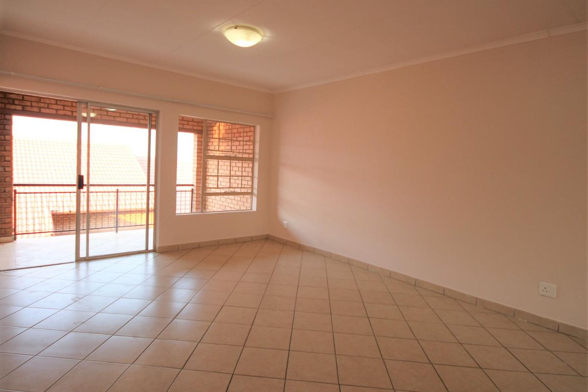 A bright, empty living room featuring neutral tiled flooring and a sliding glass door that opens onto a private balcony.