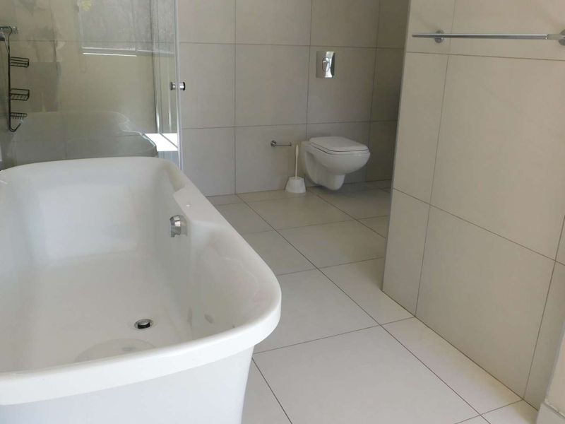 Modern bathroom featuring a freestanding bathtub, wall-mounted toilet, and a glass-enclosed shower with neutral ceramic tiling throughout.