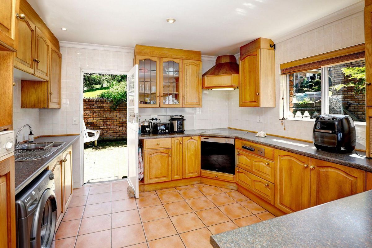 A functional kitchen featuring timber cabinetry, tiled flooring, integrated oven and hob, and direct access to an outdoor patio area.