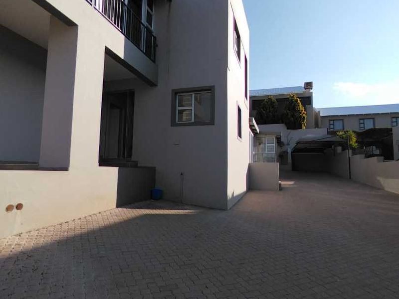 A view of the property's front exterior, featuring a paved driveway, a multi-level facade with a balcony, and a covered carport area.