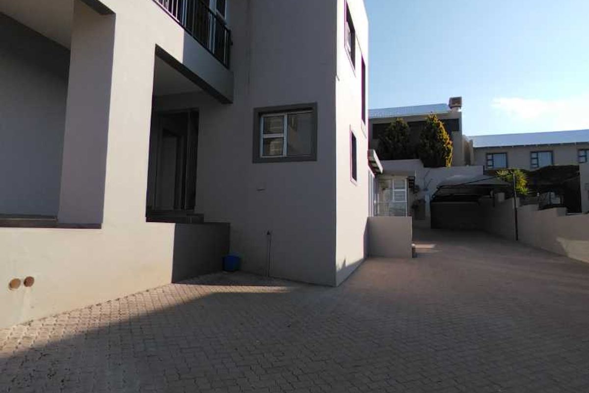 A view of the property's front exterior, featuring a paved driveway, a multi-level facade with a balcony, and a covered carport area.