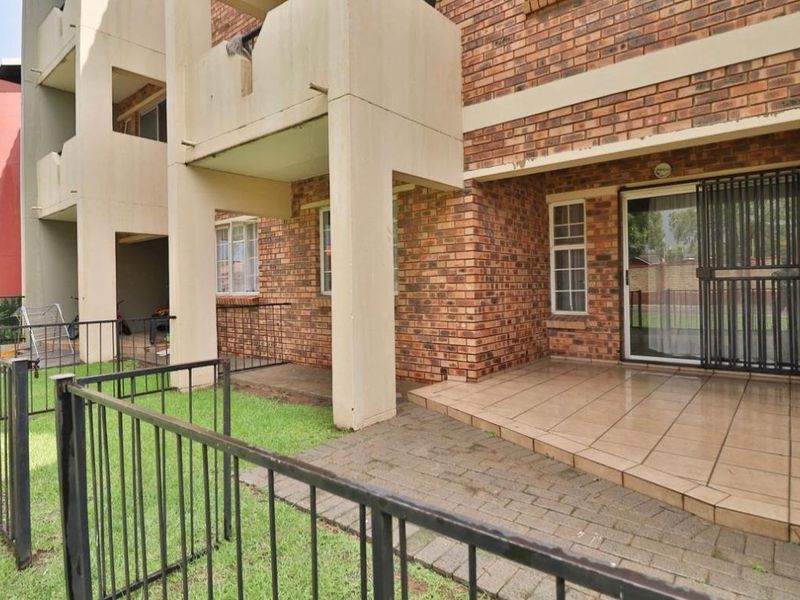 Ground floor apartment exterior featuring a private tiled patio, brick facade, and secure metal fencing overlooking a small garden area.