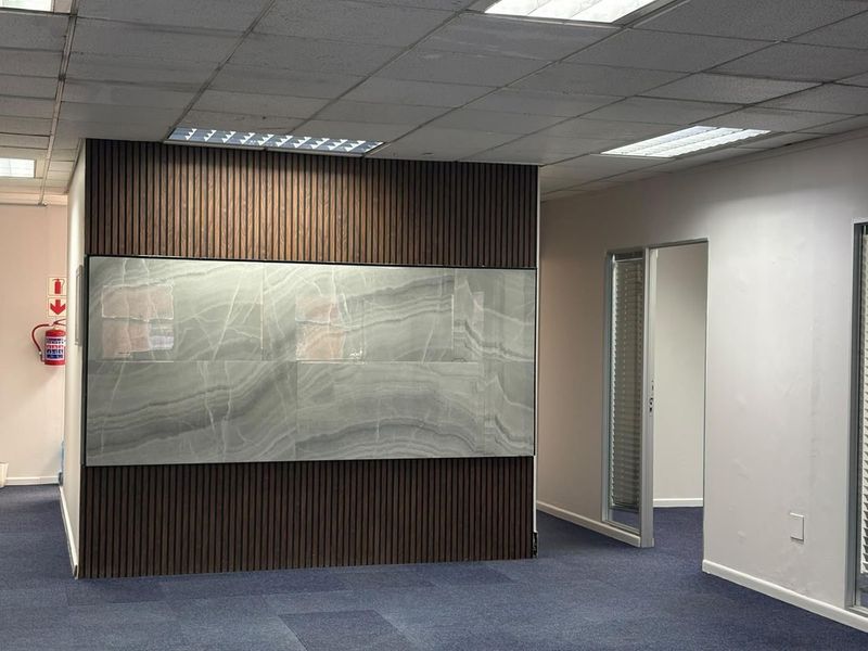 Modern office space featuring a decorative timber slat and stone feature wall, suspended ceiling, and blue carpeting.