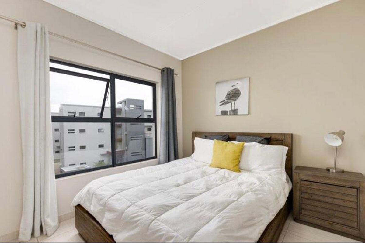 A well-maintained bedroom featuring neutral wall tones, tiled flooring, and a large aluminium-framed window providing natural light and an urban view.