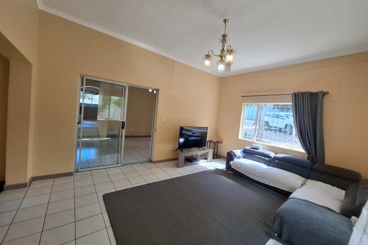 Spacious living room featuring tiled flooring, a classic chandelier, and sliding glass doors providing access to an adjacent room.