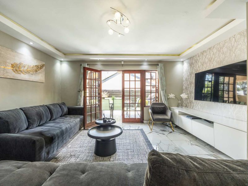 A well-maintained living room featuring marble-look floor tiles, recessed ceiling lighting with cove accents, and double french doors leading to an outdoor patio area.