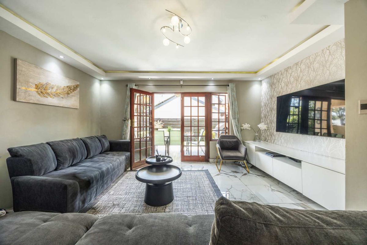 A well-maintained living room featuring marble-look floor tiles, recessed ceiling lighting with cove accents, and double french doors leading to an outdoor patio area.