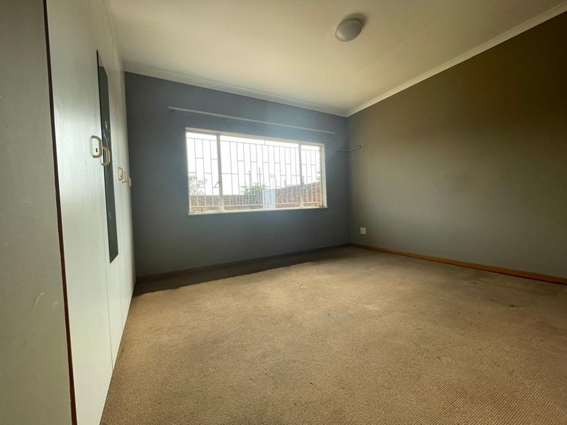 An empty bedroom featuring built-in cupboards, carpeted flooring, and a window fitted with security bars.