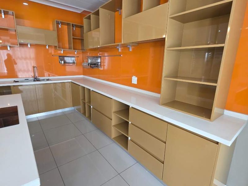 Modern kitchen featuring extensive built-in cabinetry, sleek quartz countertops, vibrant orange glass splashbacks, and high-gloss finishes throughout.