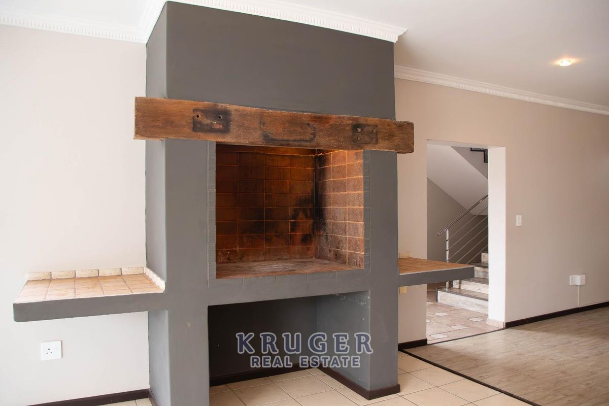 Spacious living area featuring a prominent built-in fireplace with a rustic timber mantelpiece and tiled hearth, leading to an adjacent staircase.