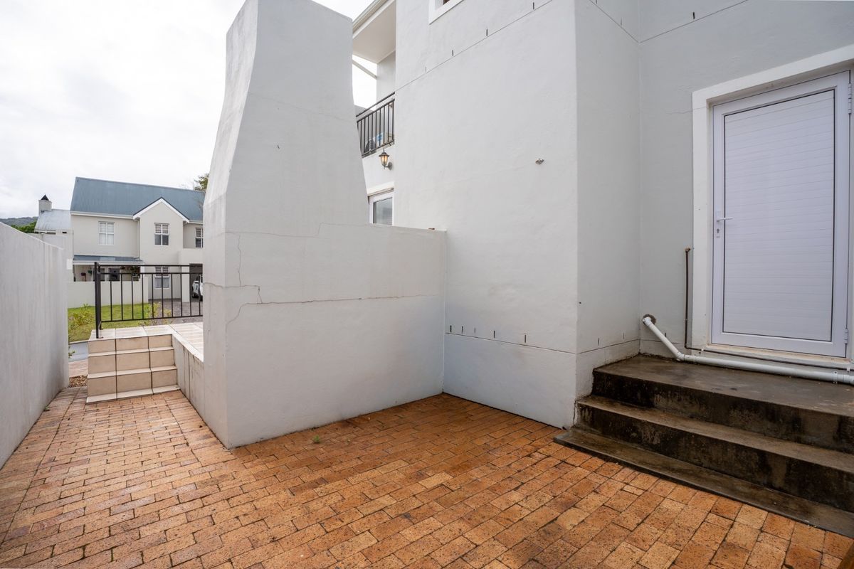 Rear exterior courtyard featuring brick paving, concrete steps, and a built-in masonry fireplace, showing signs of structural cracking in the masonry.