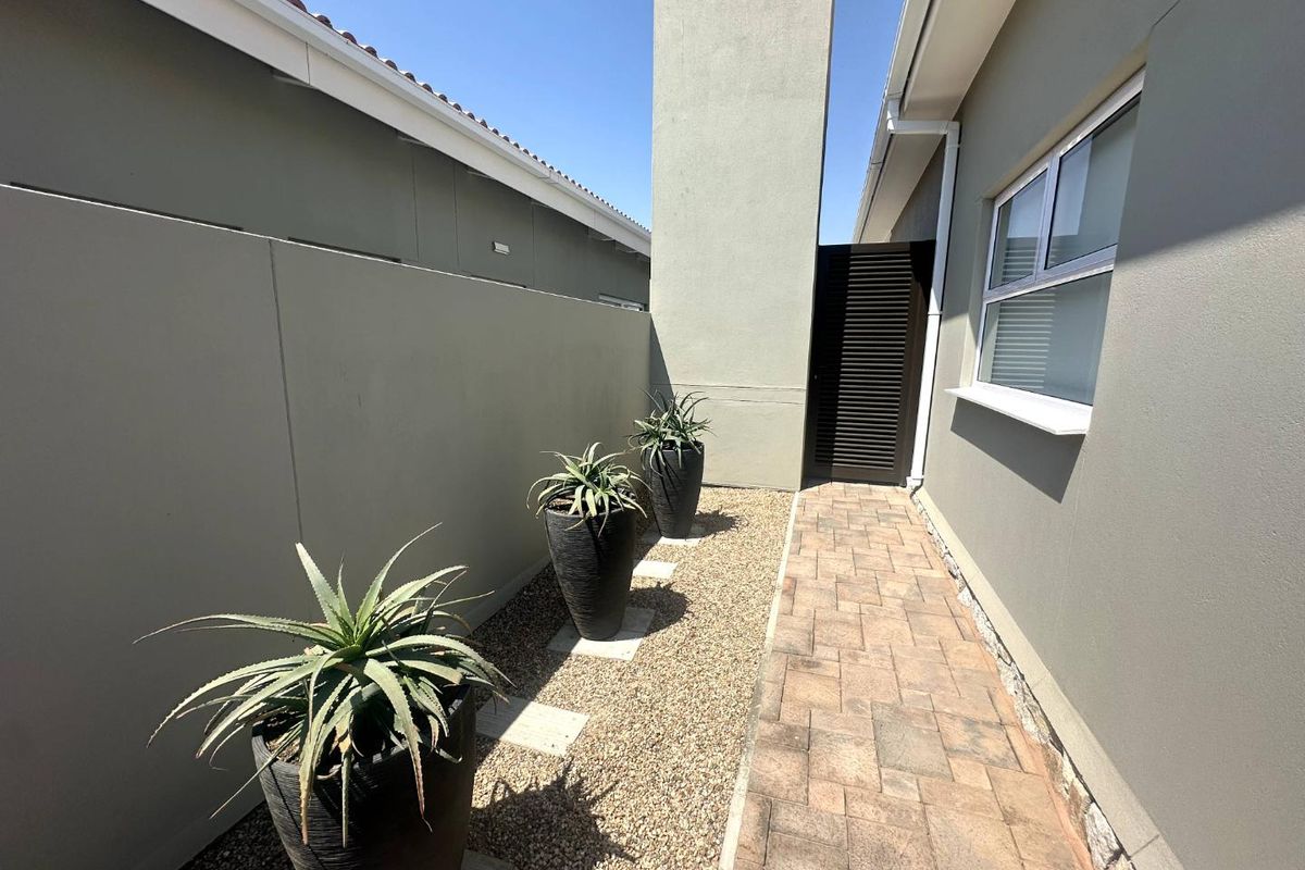 A side exterior walkway featuring paved stone paths, gravel landscaping, and a tall chimney structure along the side of the house.