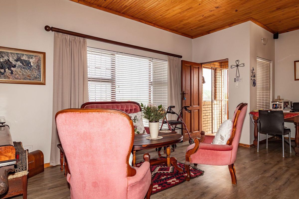 A cozy living room featuring warm timber ceilings, laminate flooring, and natural light through venetian blinds, with direct access to an outdoor area.