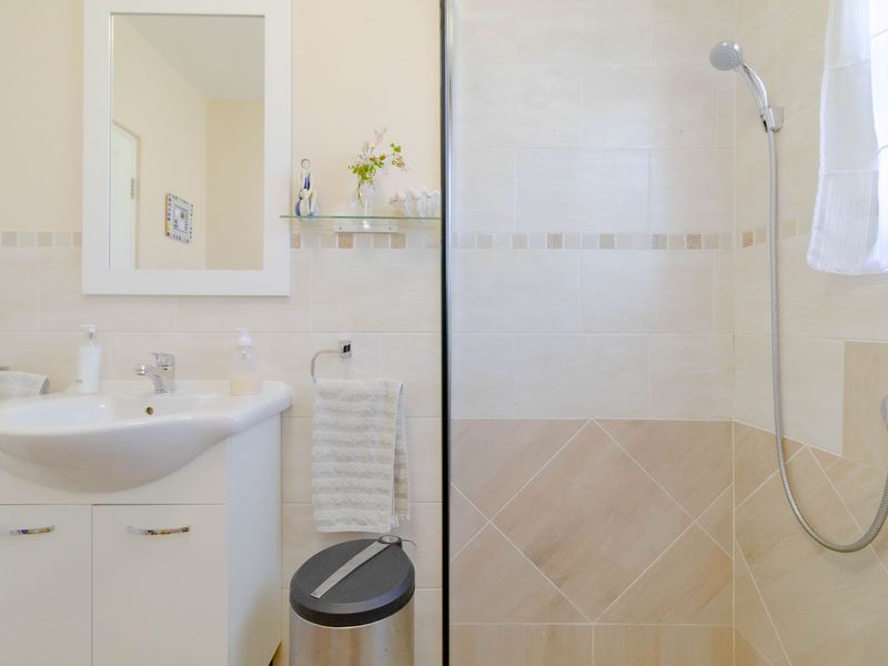 A clean, functional bathroom featuring a vanity cabinet with basin, wall-mounted mirror, and a tiled shower enclosure.