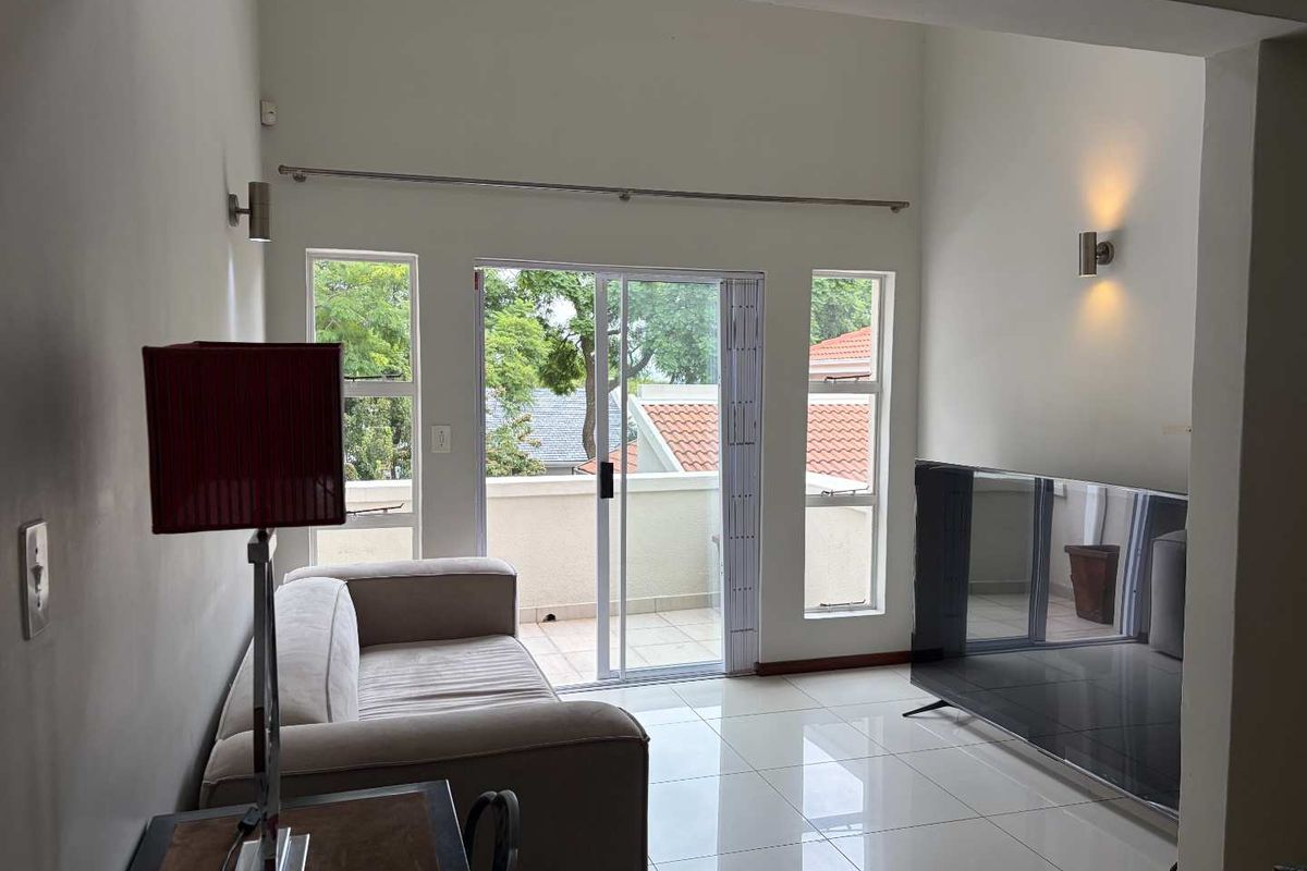 A bright living area featuring high ceilings, polished tile flooring, and sliding glass doors that open onto a private balcony.
