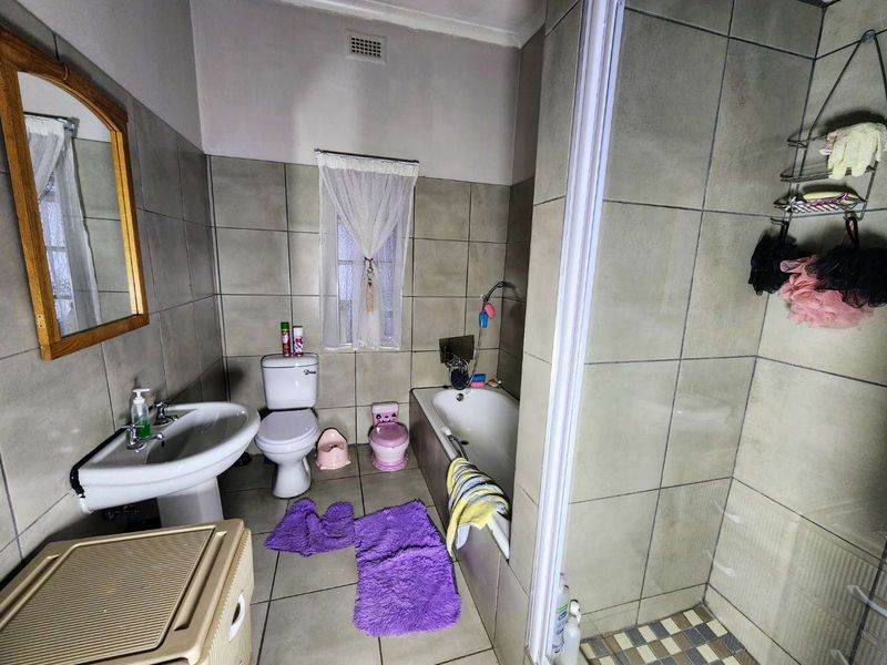 A functional bathroom featuring a pedestal basin, toilet, bathtub, and a separate shower enclosure with neutral wall and floor tiling.