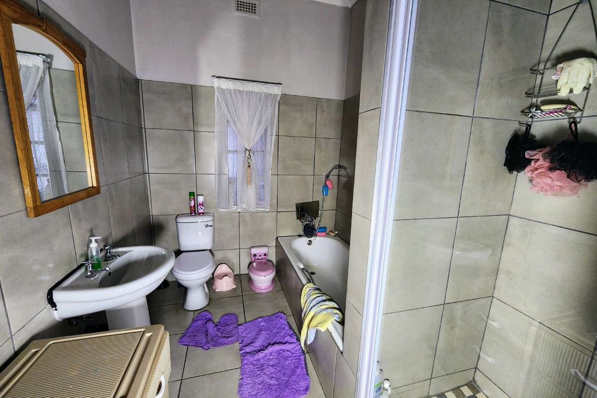 A functional bathroom featuring a pedestal basin, toilet, bathtub, and a separate shower enclosure with neutral wall and floor tiling.