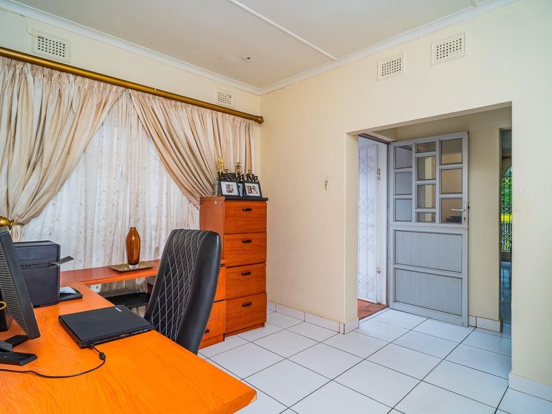 A functional office space featuring tiled flooring, neutral walls, and a secure entrance door leading to the exterior.