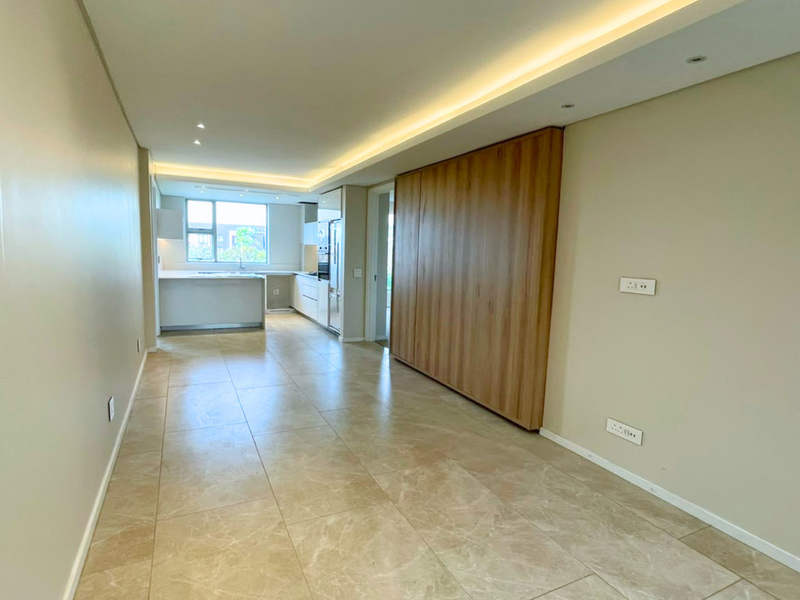 Modern open-plan living and kitchen area featuring sleek built-in cabinetry, recessed lighting, and high-quality tiled flooring in a neutral, contemporary finish.