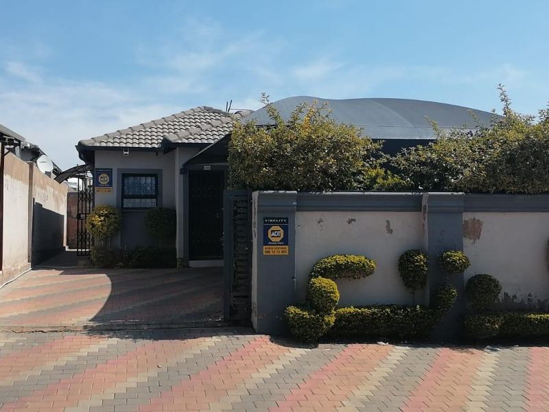 Front elevation of the property featuring a paved driveway, secure perimeter wall, and gated entrance.