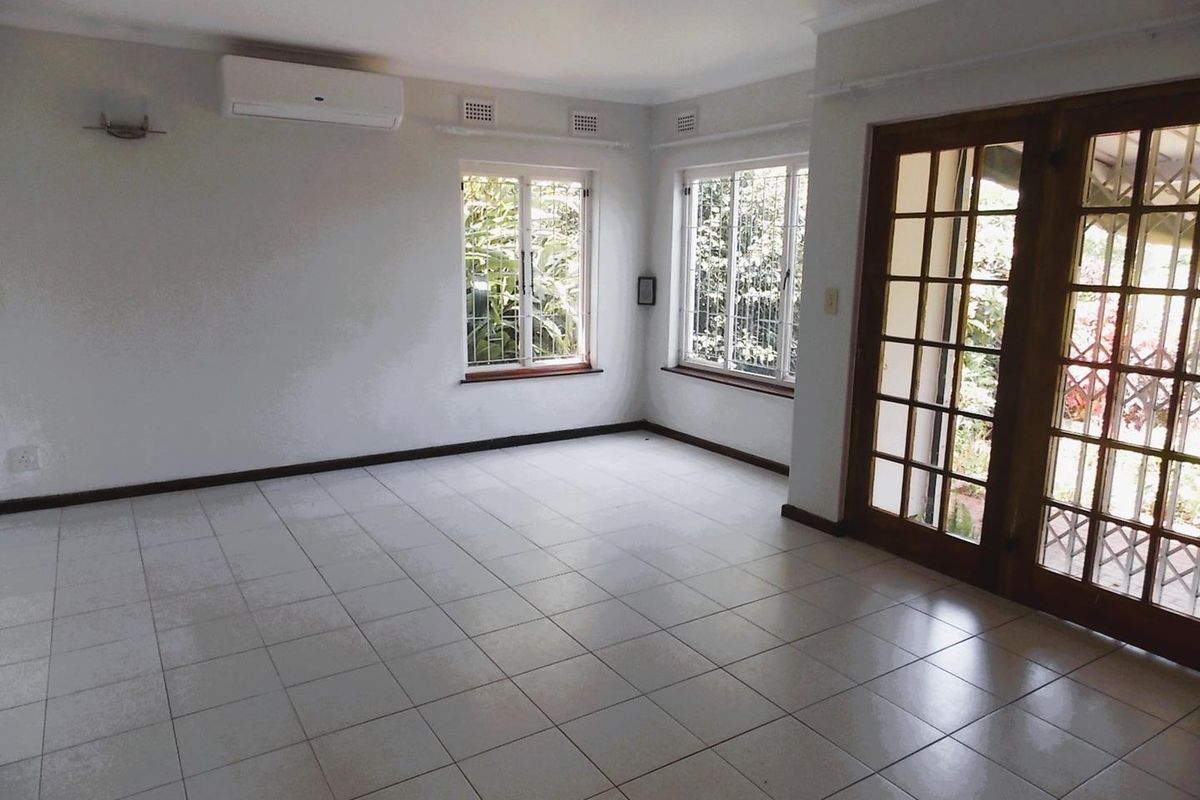 A bright, empty living room featuring tiled flooring, a wall-mounted air conditioning unit, and wooden French doors leading to an outdoor area.