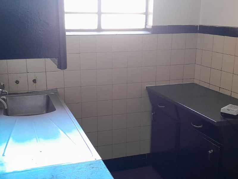 A compact kitchen area featuring a stainless steel sink, built-in cabinetry, and tiled splashbacks, offering a functional space ready for modernization.