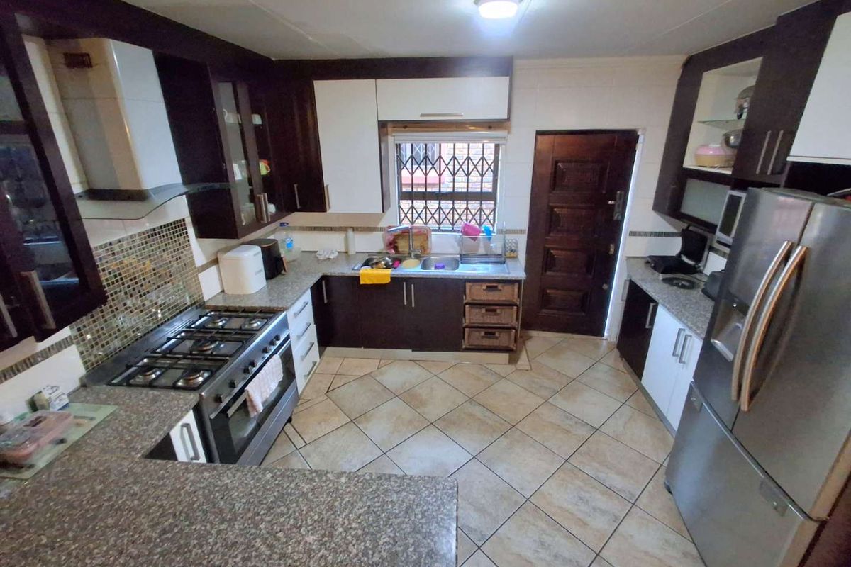 Functional kitchen featuring dark and white cabinetry, granite countertops, mosaic tile backsplash, gas stove with extractor, and tiled flooring.