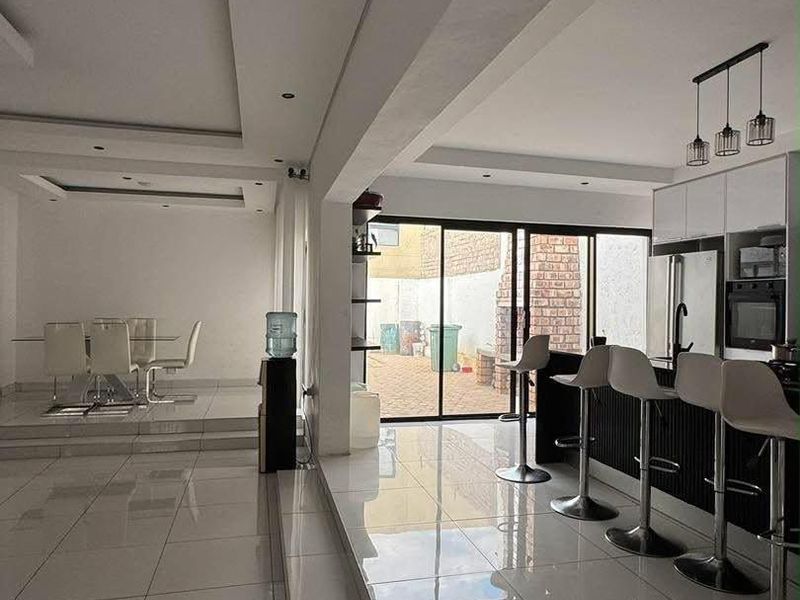 Modern open-plan living and kitchen area featuring polished porcelain tiles, a raised dining platform, and large sliding doors leading to the rear exterior.